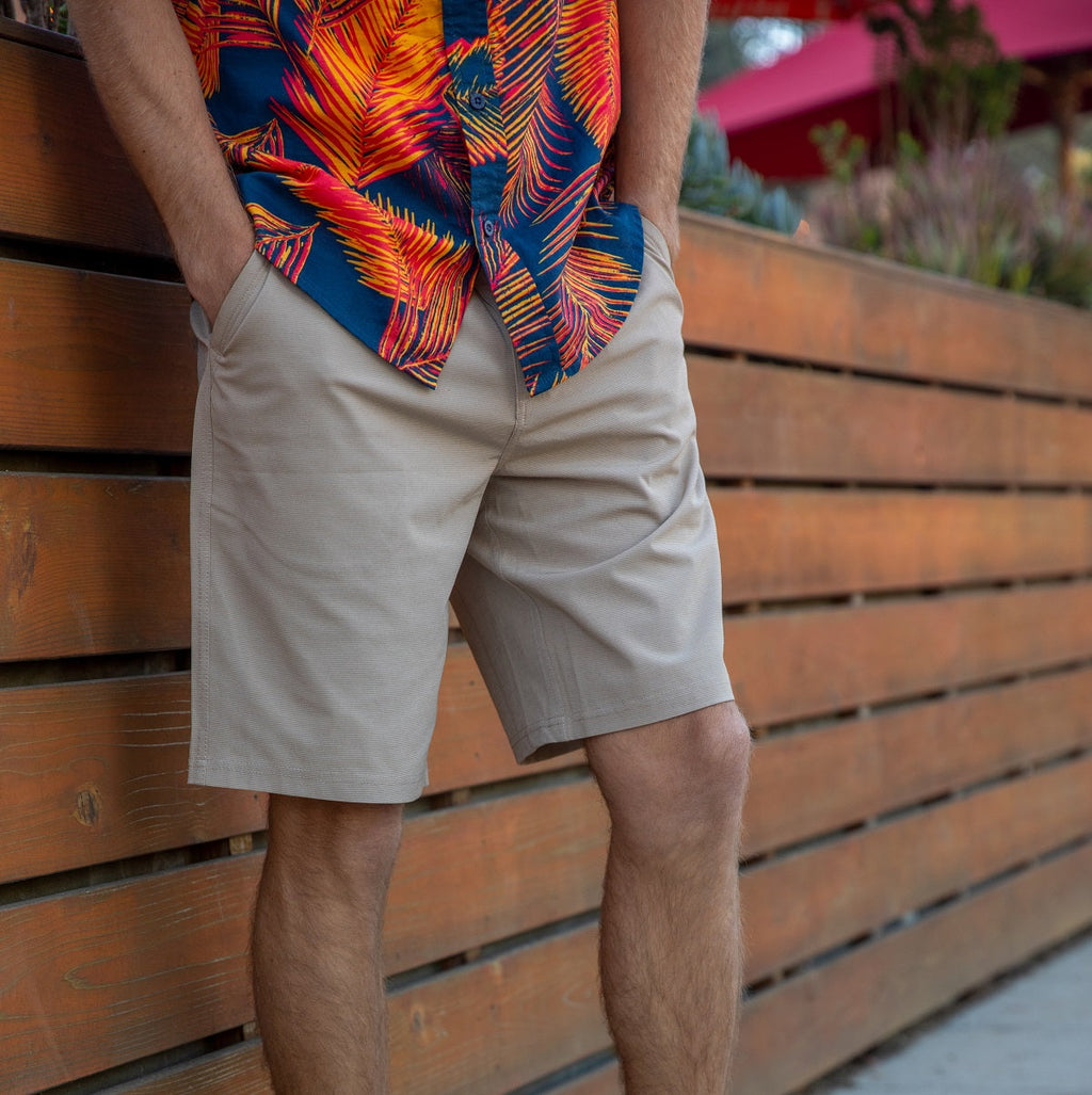 Men wearing beige Dante Walk Short standing against a wooden fence, beach-inspired casual apparel for everyday comfort.