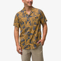 Man wearing a short-sleeve Kantis Shirt with blue and yellow leaf print, front view, hands in pockets, beach-inspired comfort apparel.