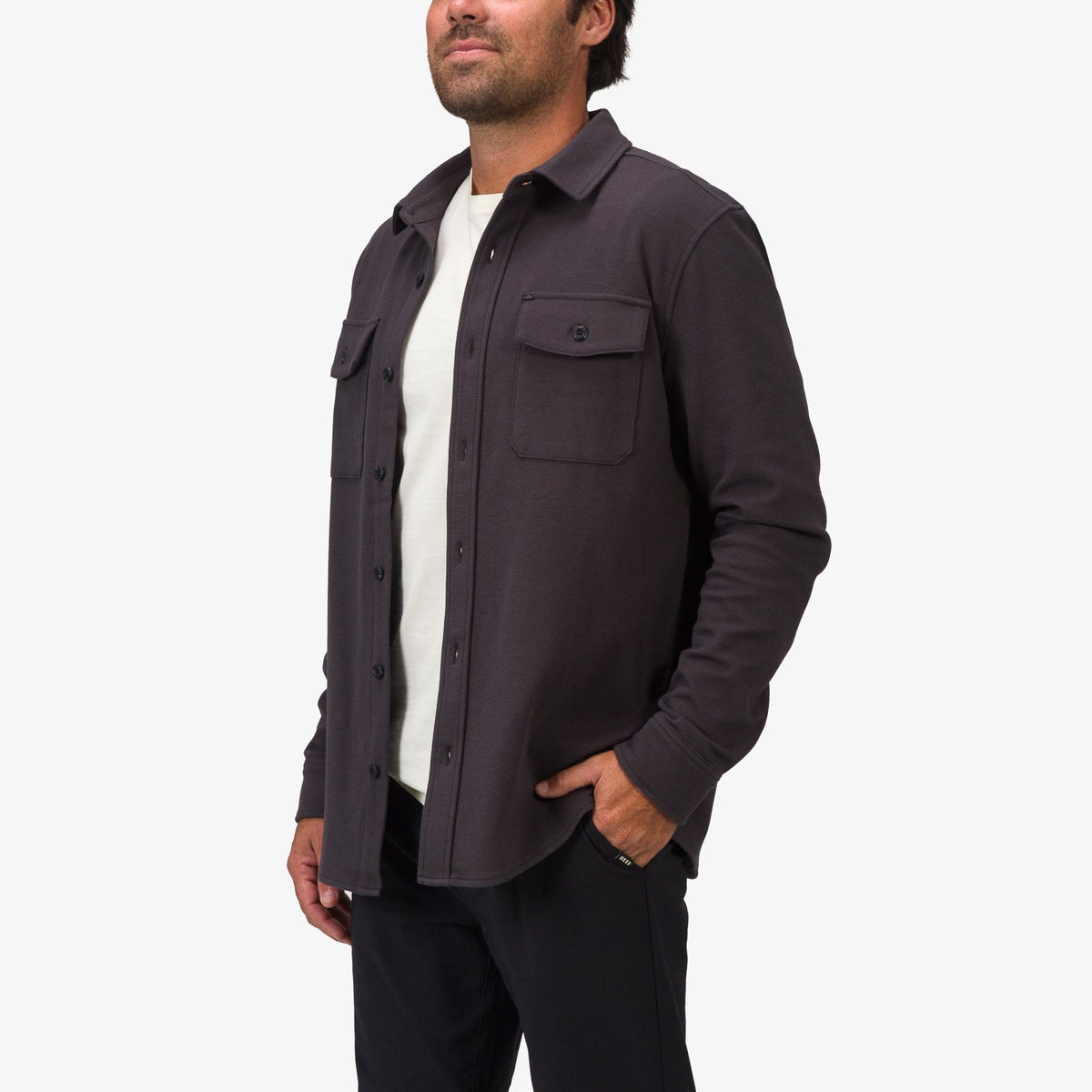 Man wearing a dark Raymond Ls Shirt with front chest pockets, styled open over a white tee, showing comfort-focused casual wear.