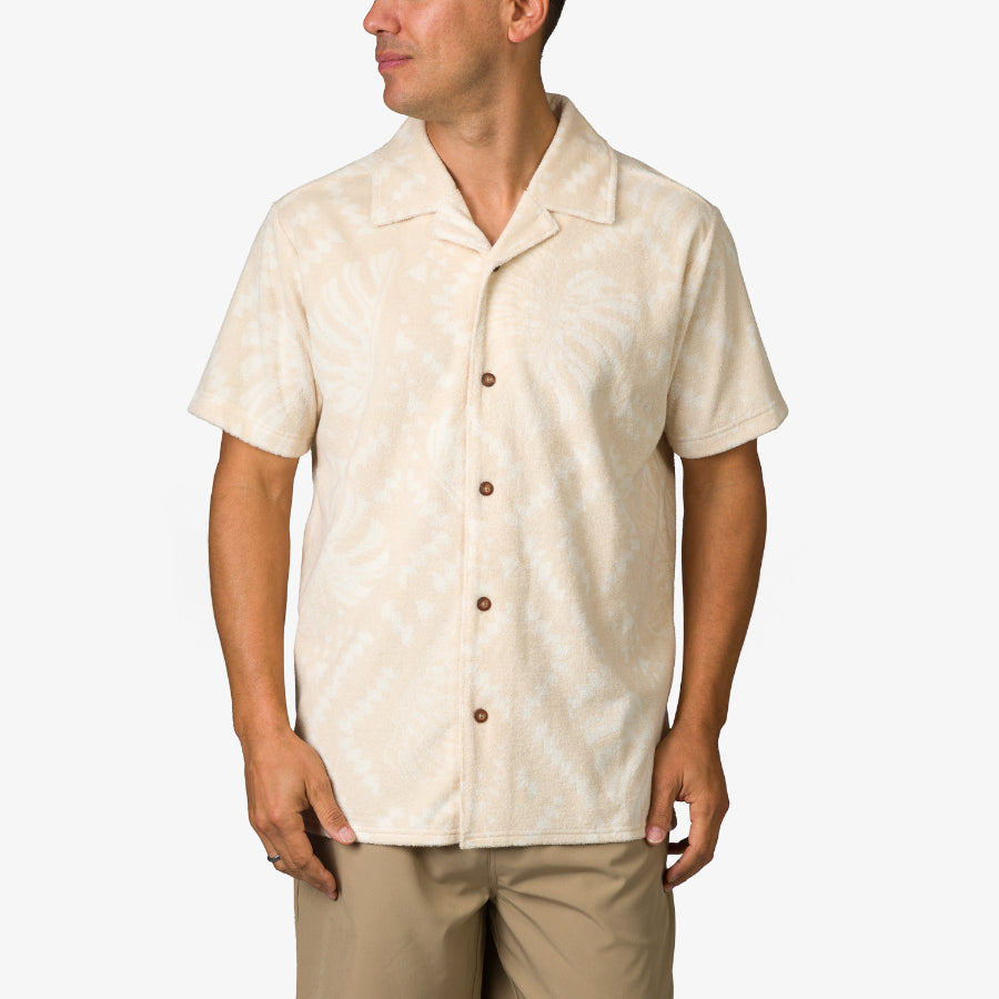 Man wearing a beige Novak Camp Shirt with subtle leaf patterns, front buttoned, facing left in a relaxed pose