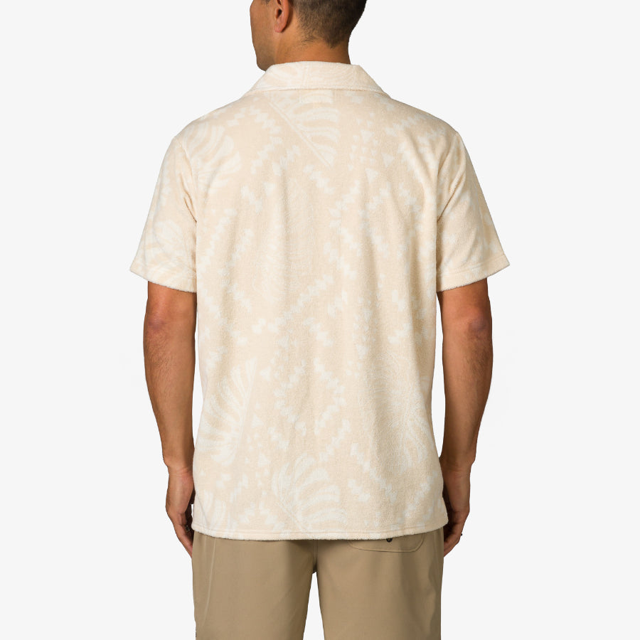Man wearing Novak Camp Shirt in light beige with subtle tropical pattern, shown from back for relaxed beach style.