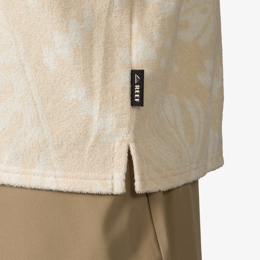 Close-up of the lower side hem of the Novak Camp Shirt in beige terry fabric with REEF label, showcasing beach-inspired comfort.