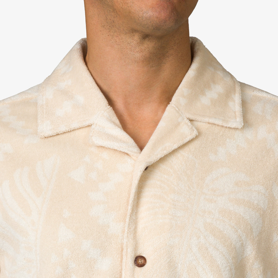 Close-up of a man wearing a beige Novak Camp Shirt with a subtle pattern and a classic camp collar design.