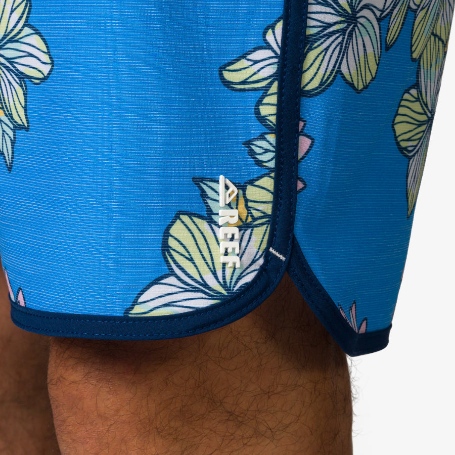 Close-up of the Tanner Boardshort's lower leg area in azure with floral print and REEF logo, showing water-friendly fabric.
