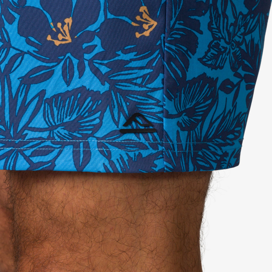 Close-up of the lower hem of the Felix Boardshort in blue with tropical print worn on a man's leg, showcasing comfort and style.
