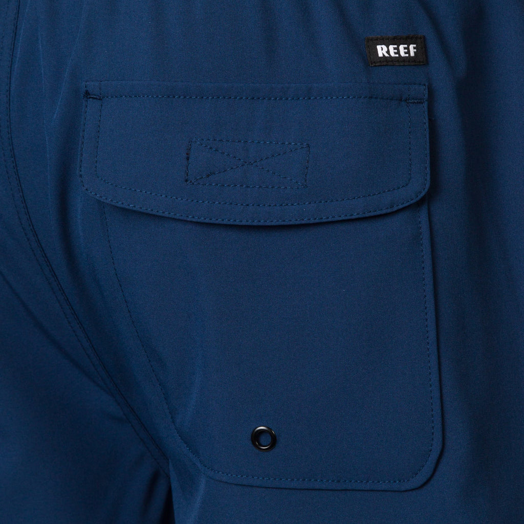 Close-up of the back pocket on the Garland Hybrid Short in navy blue, highlighting the REEF logo and durable stitching.