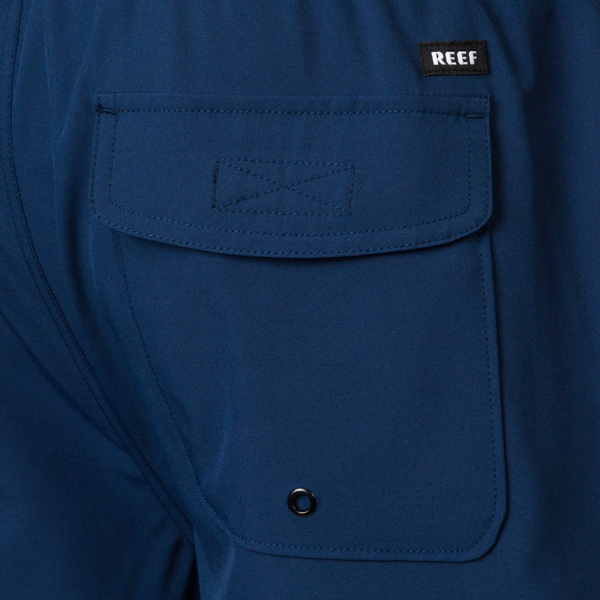Close-up of the back pocket on the Garland Hybrid Short in navy blue, highlighting the REEF logo and durable stitching.