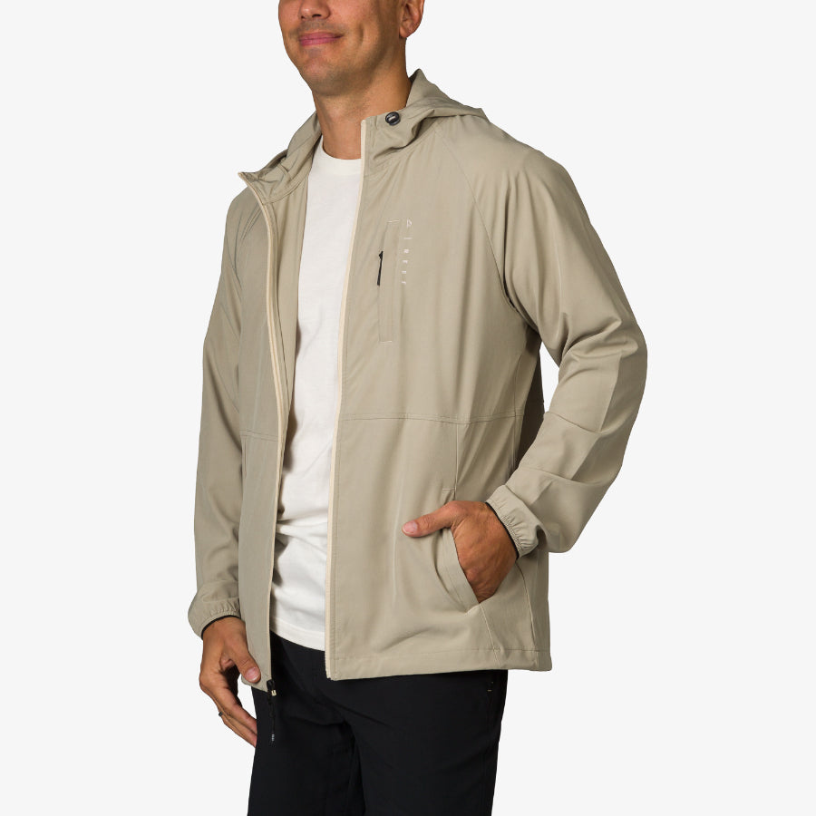 Man wearing Garvey Jacket in beige facing left with hood up, hand in pocket, showcasing lightweight, comfortable beach apparel.