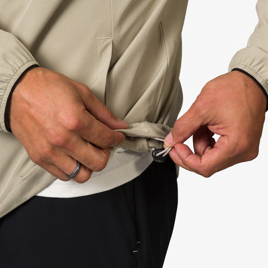 Close-up of hands adjusting the hem toggle on a beige Garvey Jacket, designed for men with beach-inspired comfort.