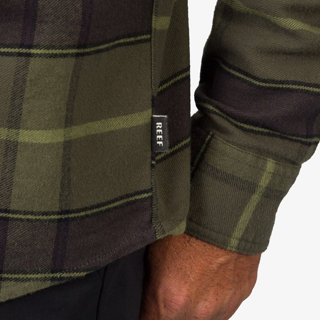 Close-up of the cuff and side seam tag on the olive Anders Long Sleeve Woven Shirt, highlighting comfort and durability.