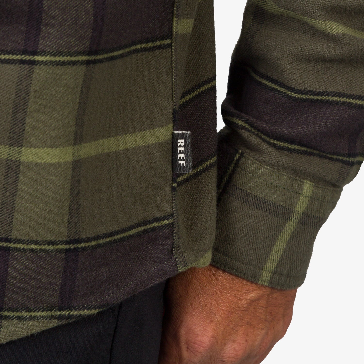 Close-up of the cuff and side seam tag on the olive Anders Long Sleeve Woven Shirt, highlighting comfort and durability.