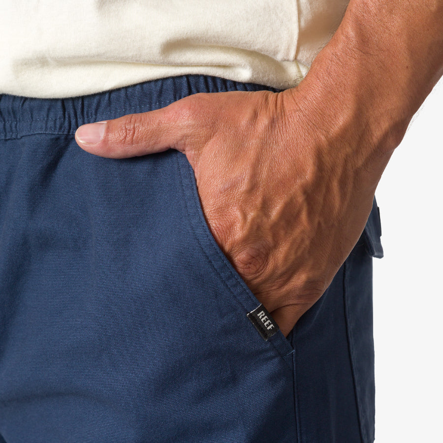Close-up of a man's hand in the right pocket of navy blue Matthew Twill Pant with REEF tag visible