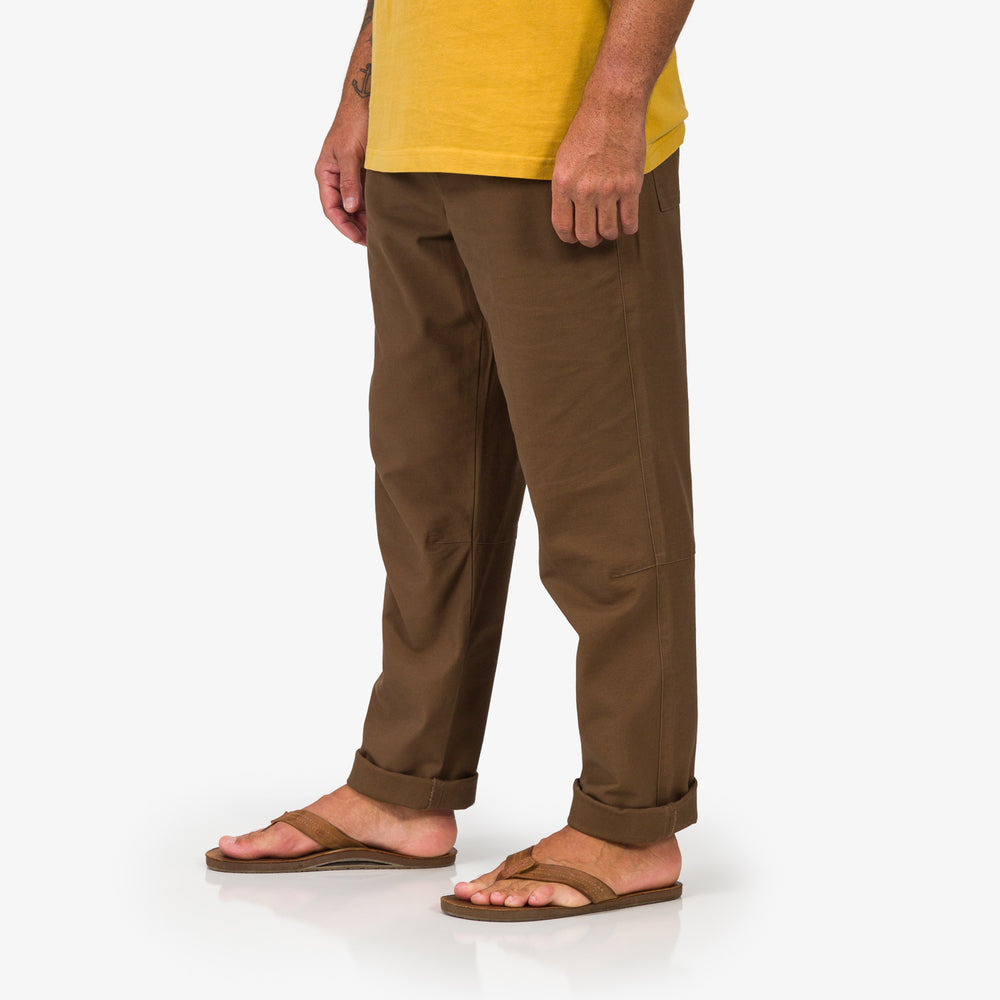 Side view of men's Matthew Twill Pant in brown paired with flip flops facing forward, highlighting comfort and beach style.
