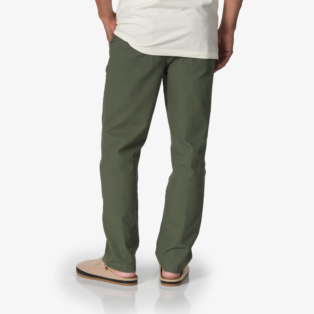Back view of a man wearing Matthew Twill Pant in thyme green, paired with beige surf-inspired sandals facing right.