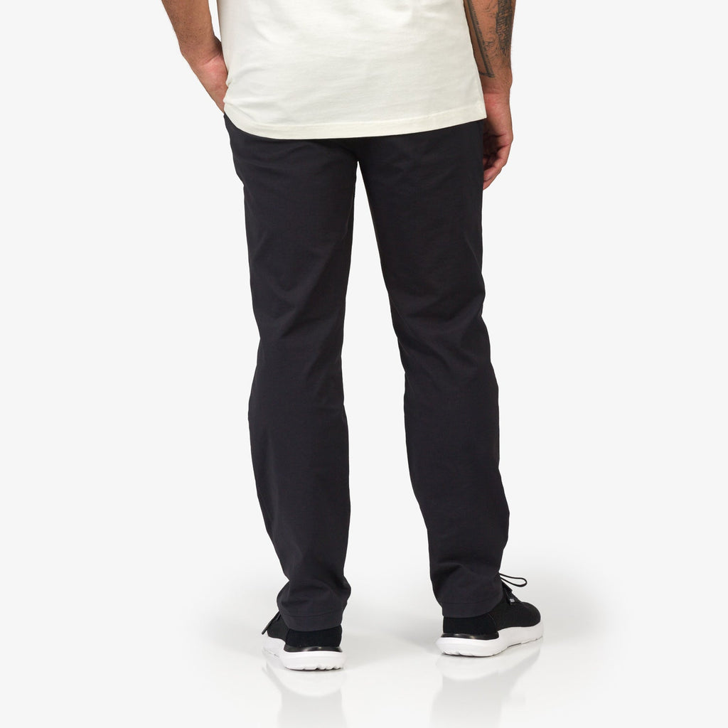 Rear view of men’s Carrick Stretch Pant in black, paired with black sneakers facing backward, comfort-focused for active lifestyles.