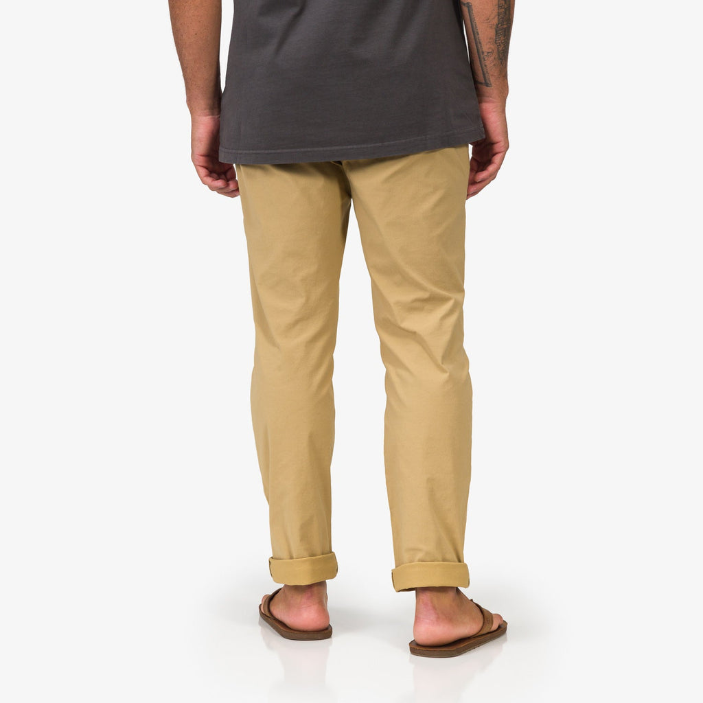Rear view of men wearing Carrick Stretch Pant in tan paired with beach-inspired sandals facing away, highlighting casual comfort.