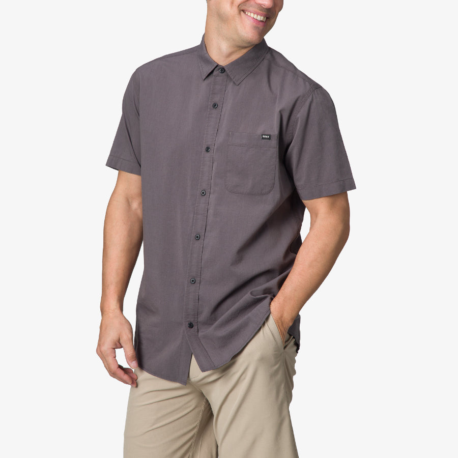 Men wearing Collins Ss Wvn Shirt in grey, standing with hands in pockets, showcasing beach-inspired casual comfort.