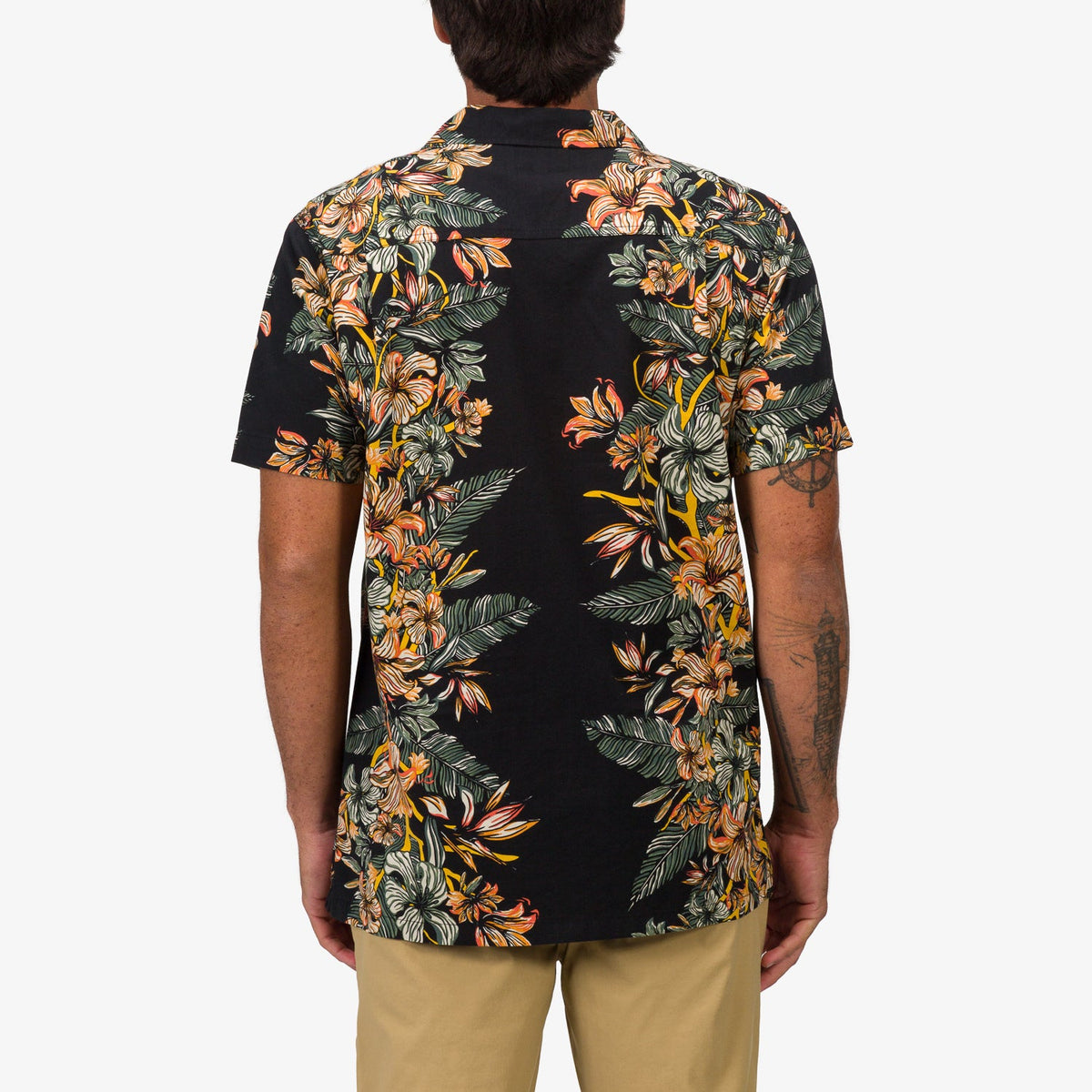 Back view of a man wearing the Drift Ss Camp Shirt with vibrant orange and green floral print on black fabric, beach-inspired apparel.