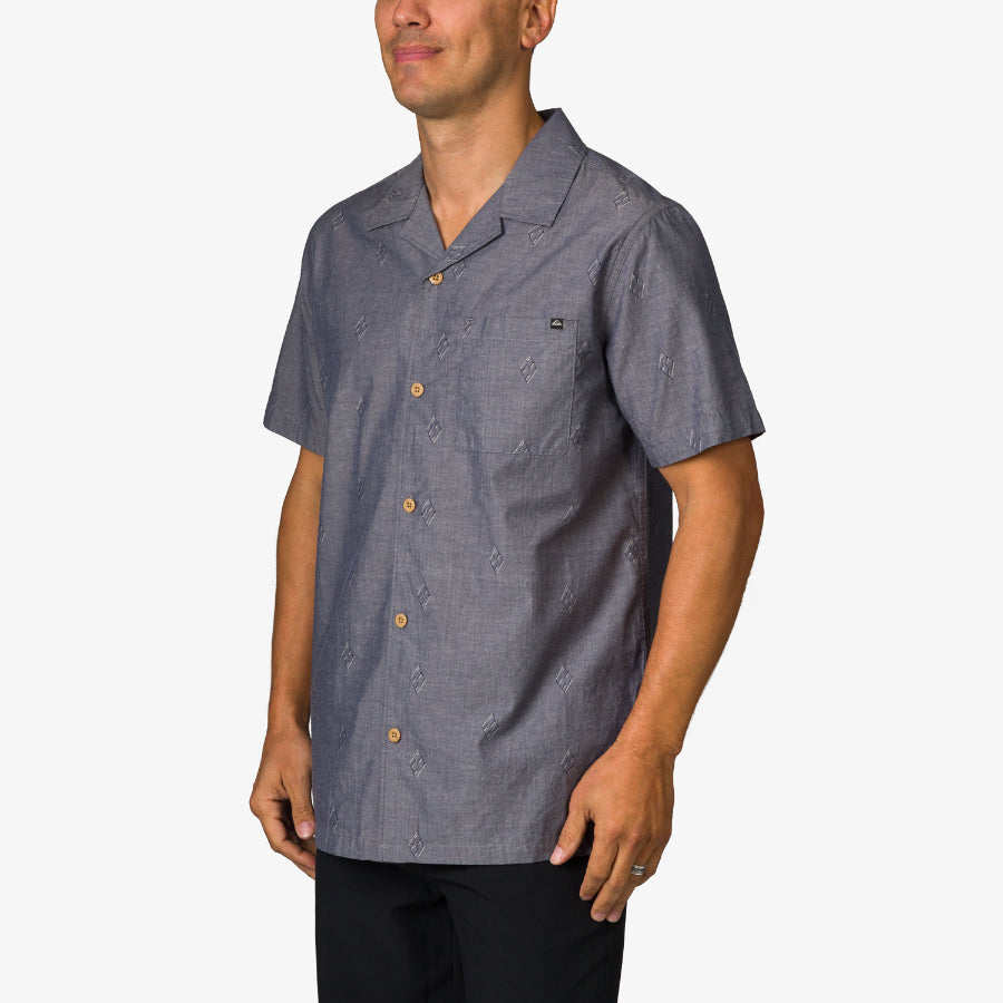 Man wearing a blue Harold Camp Shirt facing left, showing front and side with short sleeves and button closure.