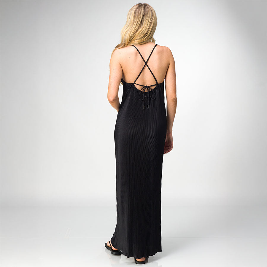Woman wearing black Plisse Dress facing away, showing back detail with thin crossed straps and tie closure, standing in sandals.