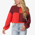 Woman wearing a red and burgundy color-block Carrie Sweater with long sleeves, shown from waist up, casual beach-inspired comfort.