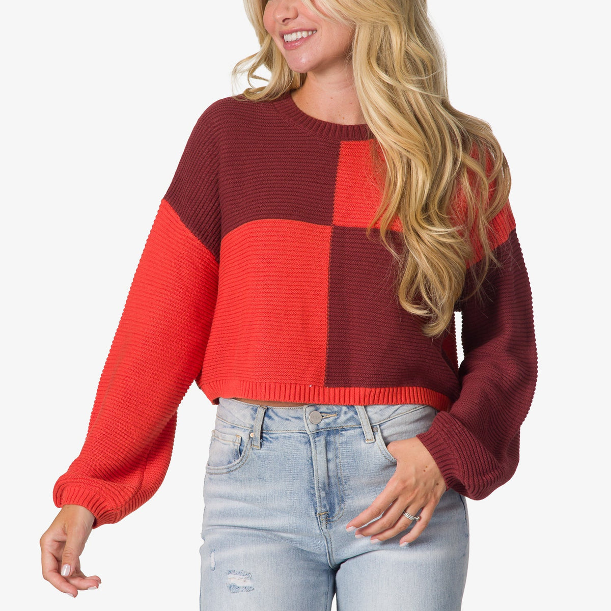 Woman wearing a red and burgundy color-block Carrie Sweater with long sleeves, shown from waist up, casual beach-inspired comfort.