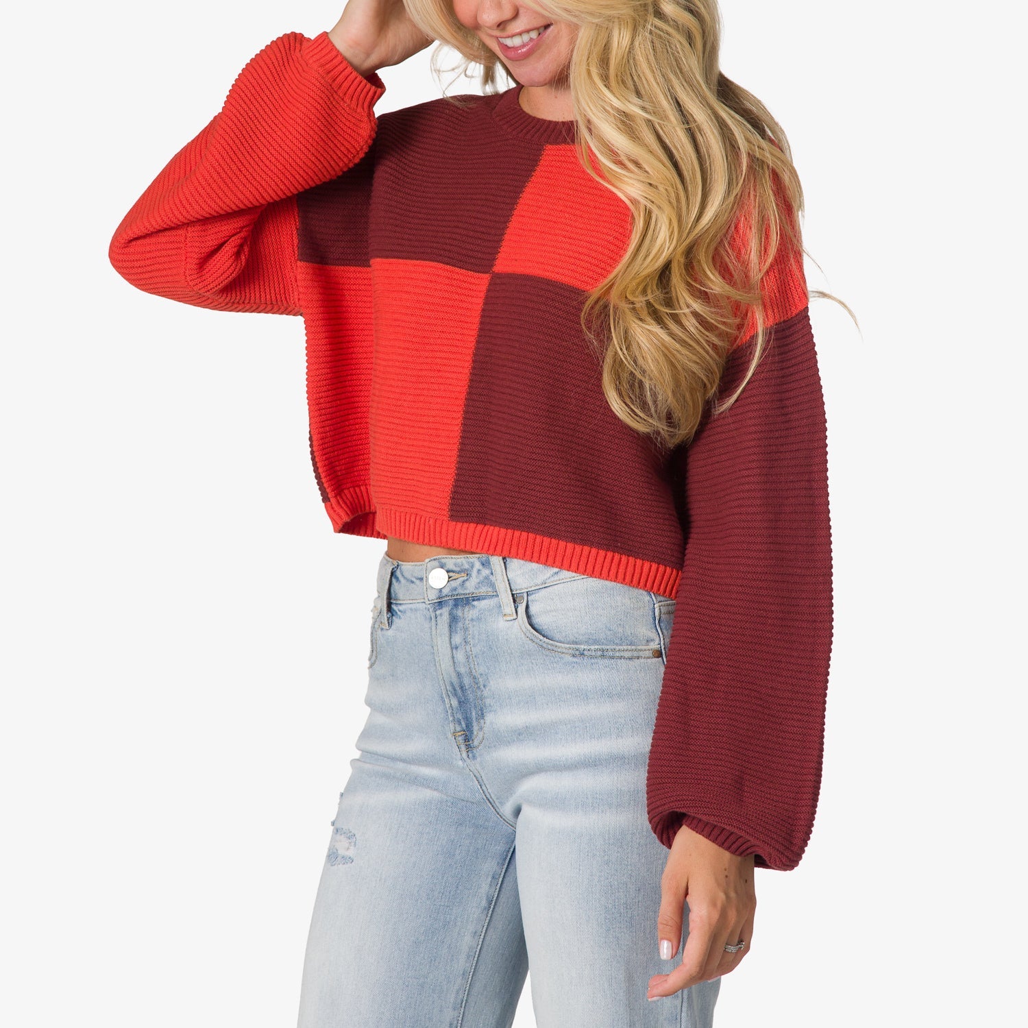 Woman wearing the Carrie Sweater, front view, with colorblock red and burgundy knit and loose sleeves.