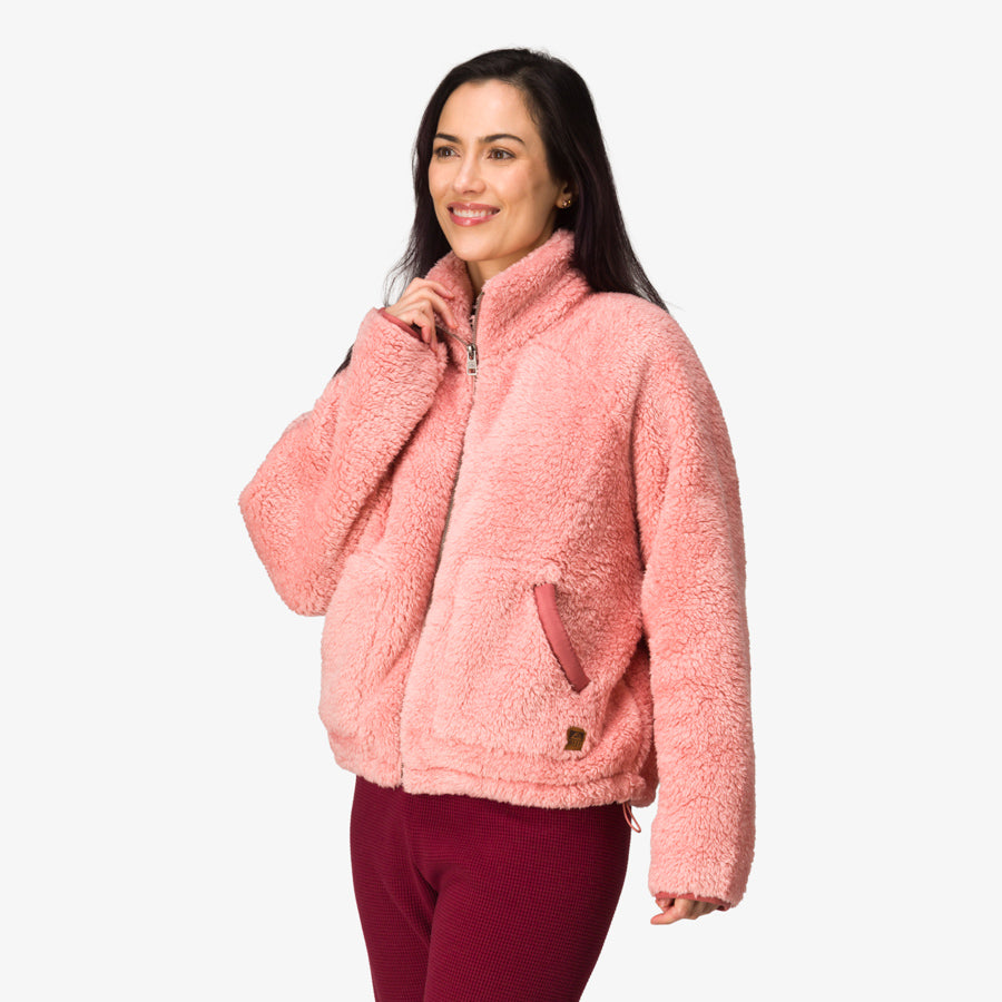 Woman wearing a pink Pilot Sherpa Jacket facing slightly left, showing front and left side with hand near collar.