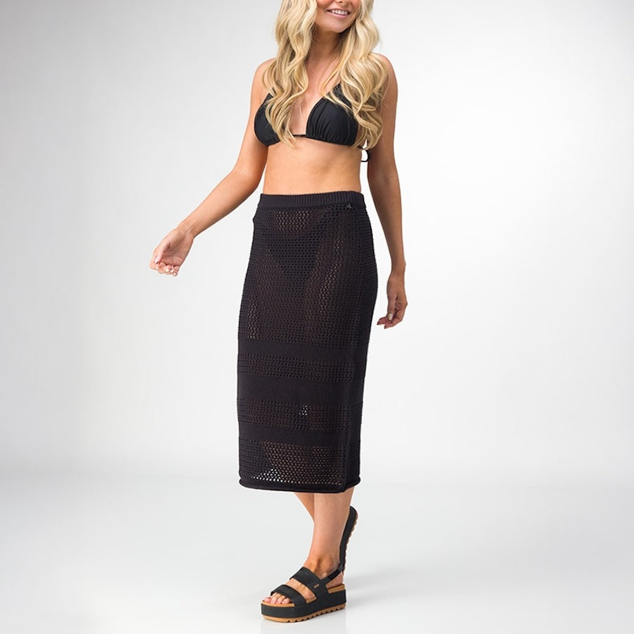 Woman wearing Mika Sweater Skirt in black with black sandals facing right, showcasing beach-inspired comfort style.
