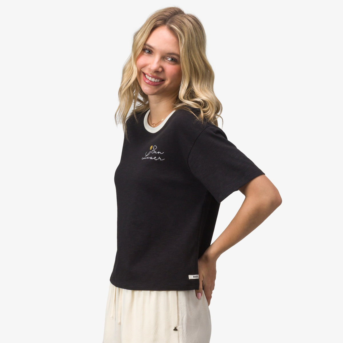 Woman wearing black Sun Lover Ringer Tee with white collar and embroidered logo, smiling in a relaxed pose, side view.