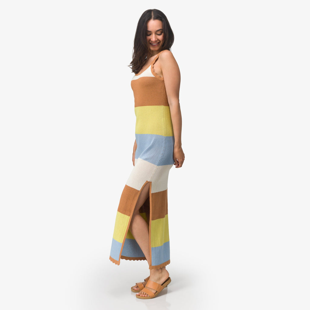 Woman wearing a striped brown, yellow, blue, and white Gia Maxi Dress with sandals facing left, side view, smiling