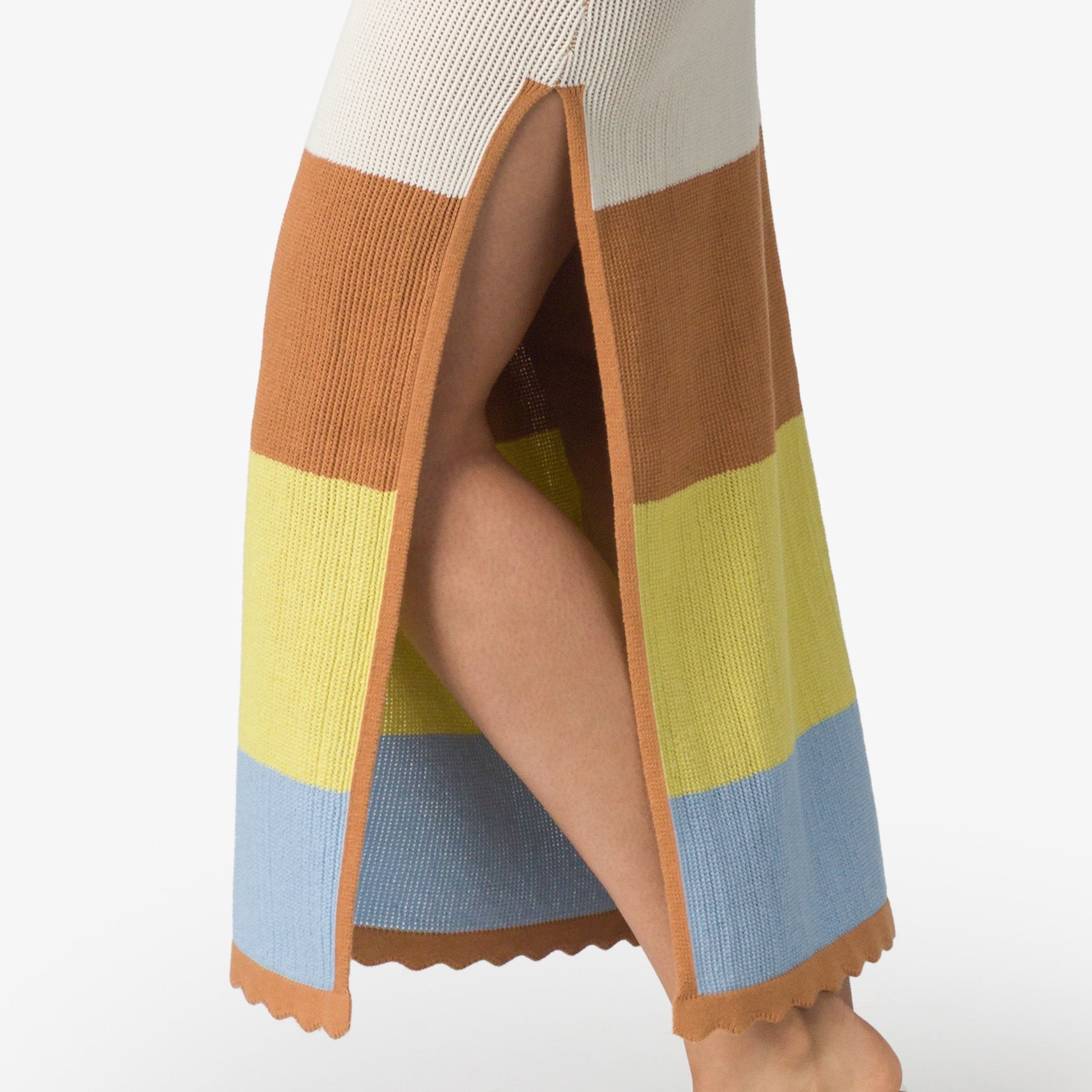 Close-up of the Gia Maxi Dress side slit showing striped knit fabric in neutral, brown, yellow, and blue tones on woman's leg.