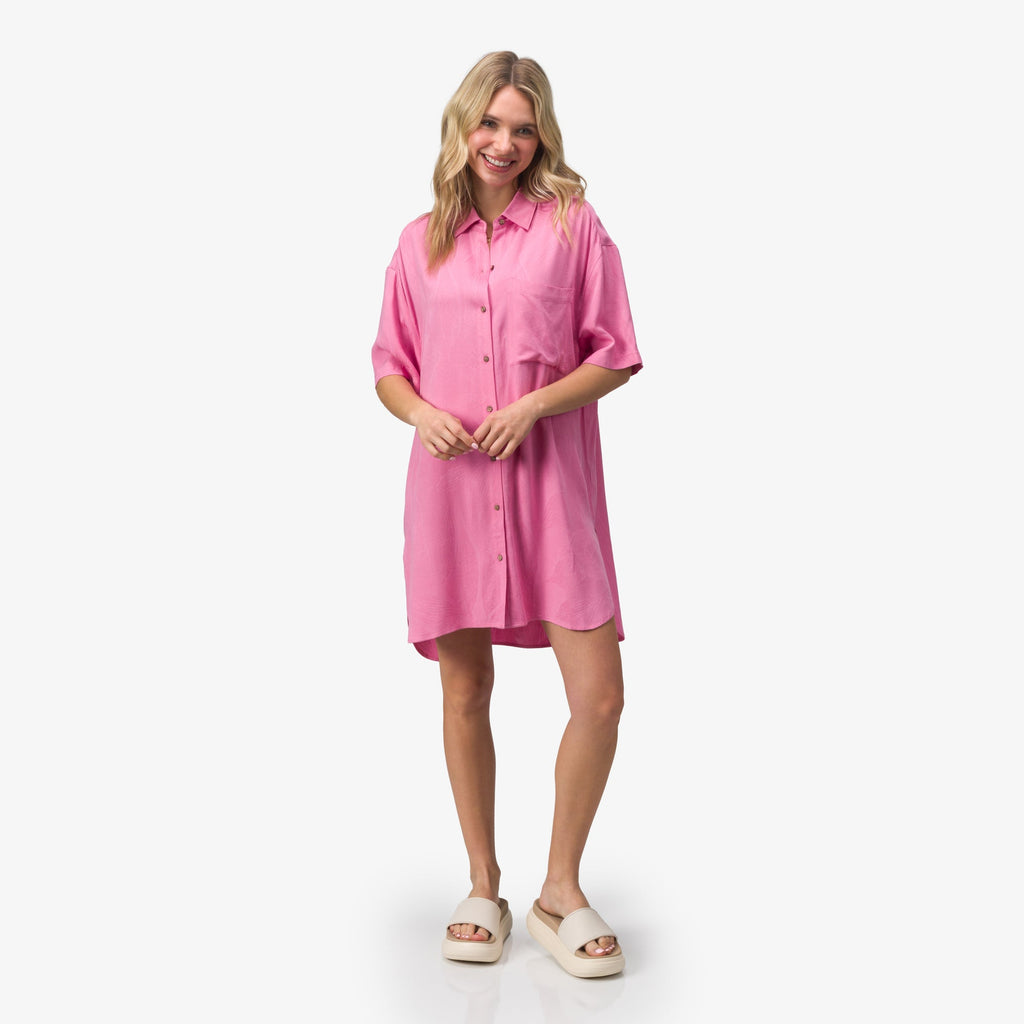 Woman wearing a pink Ollie Shirt Dress standing with beige slides facing forward, surf-inspired comfort and casual style.
