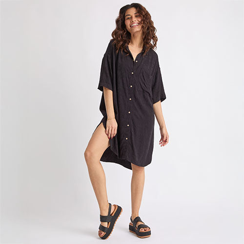 Woman wearing black Ollie Shirt Dress with short sleeves and front buttons, paired with black platform sandals facing right side.