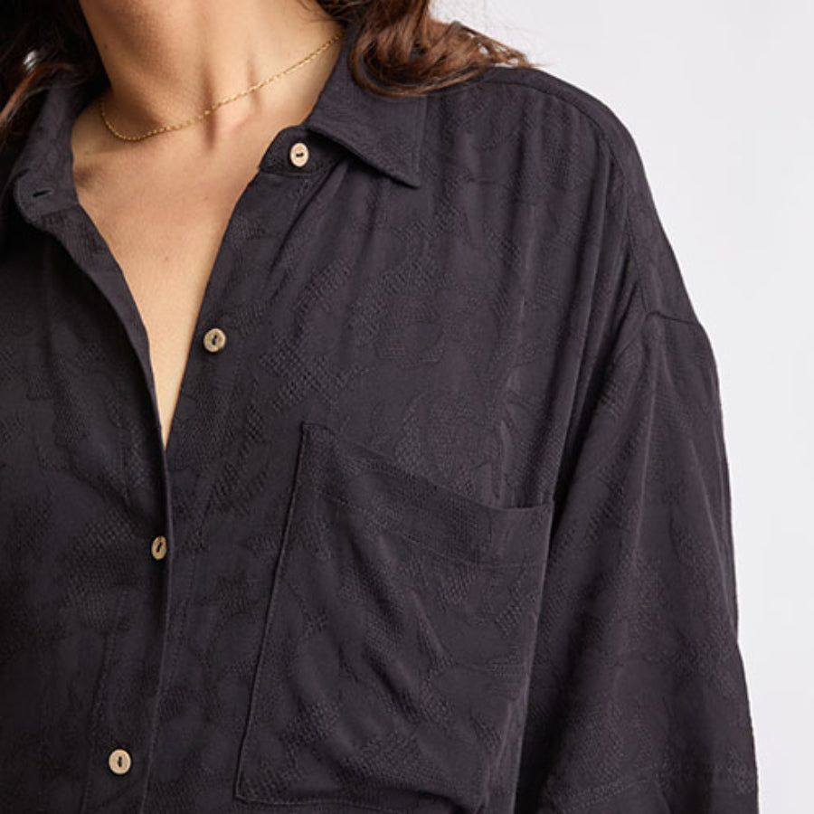 Close-up of the upper front and shoulder of the Ollie Shirt Dress in dark textured fabric for comfortable beachwear.
