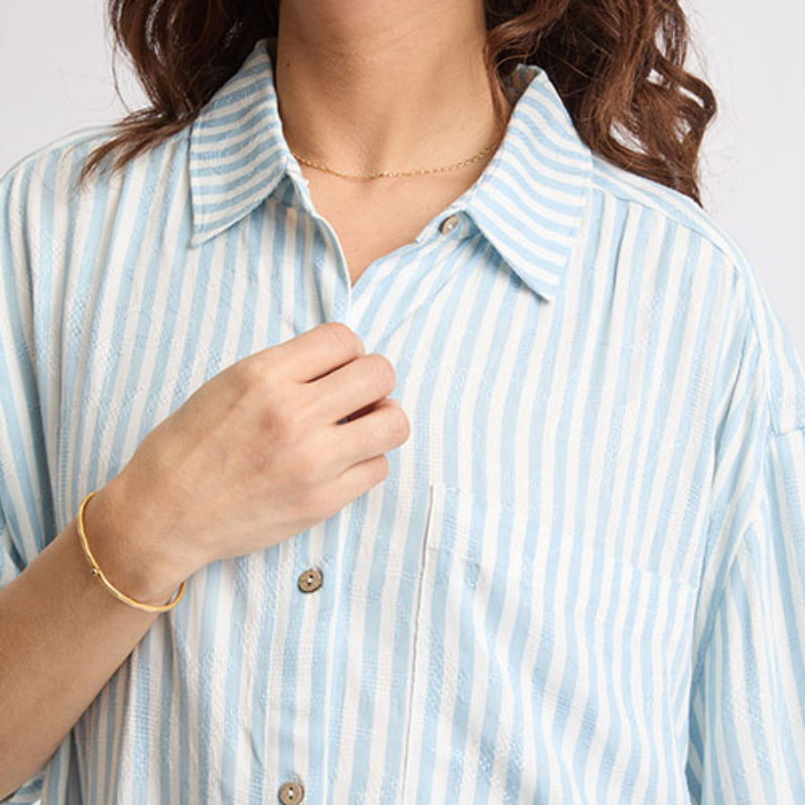 Close-up of a woman adjusting the collar of the Ollie Striped Shirt Dress with light blue and white stripes.