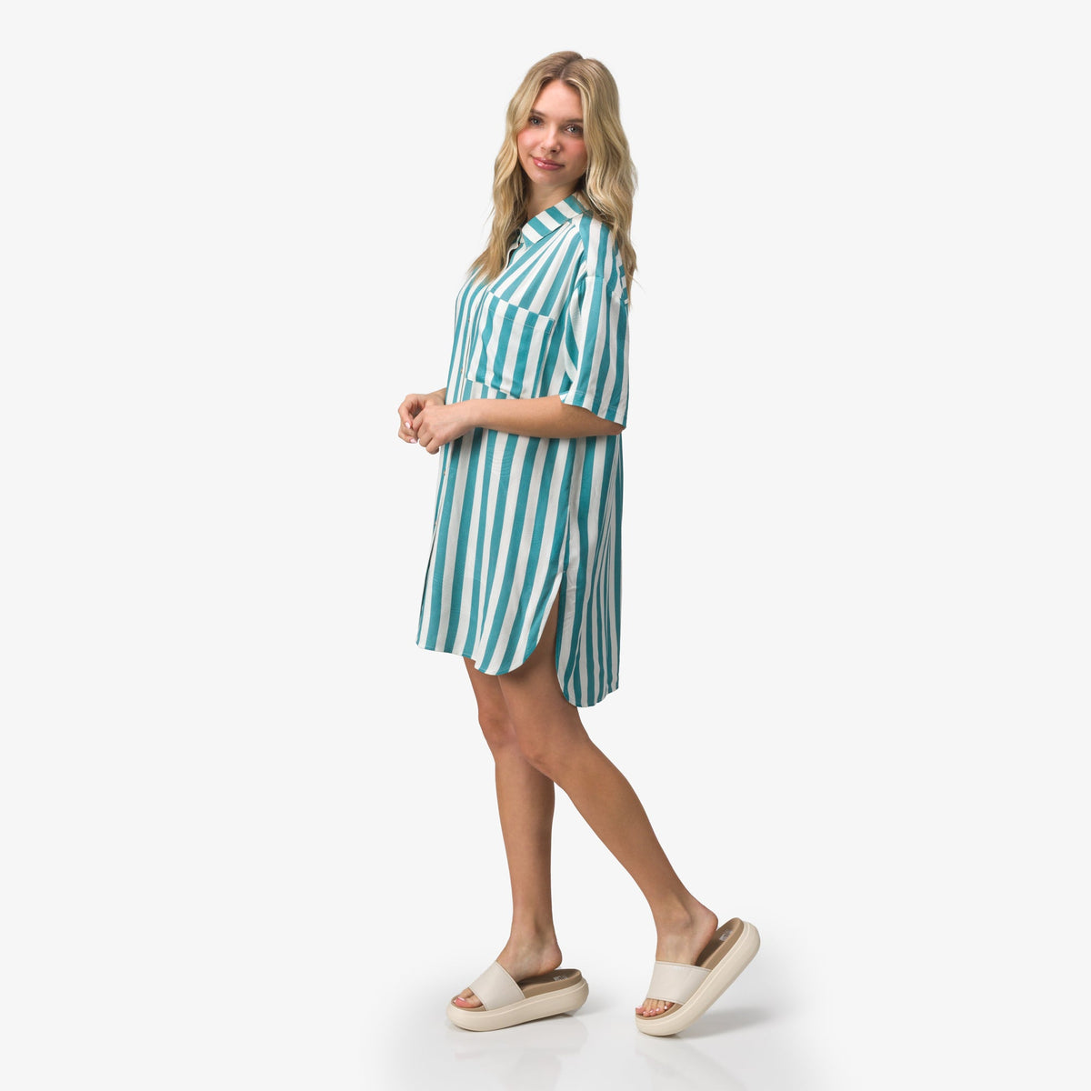 Woman wearing a striped Ollie Shirt Dress facing left, paired with beige slides showcasing beach-inspired comfort and support.