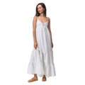 Woman wearing white Yuni Maxi Dress, standing and holding a dress hem, styled with tan sandals for beach comfort.