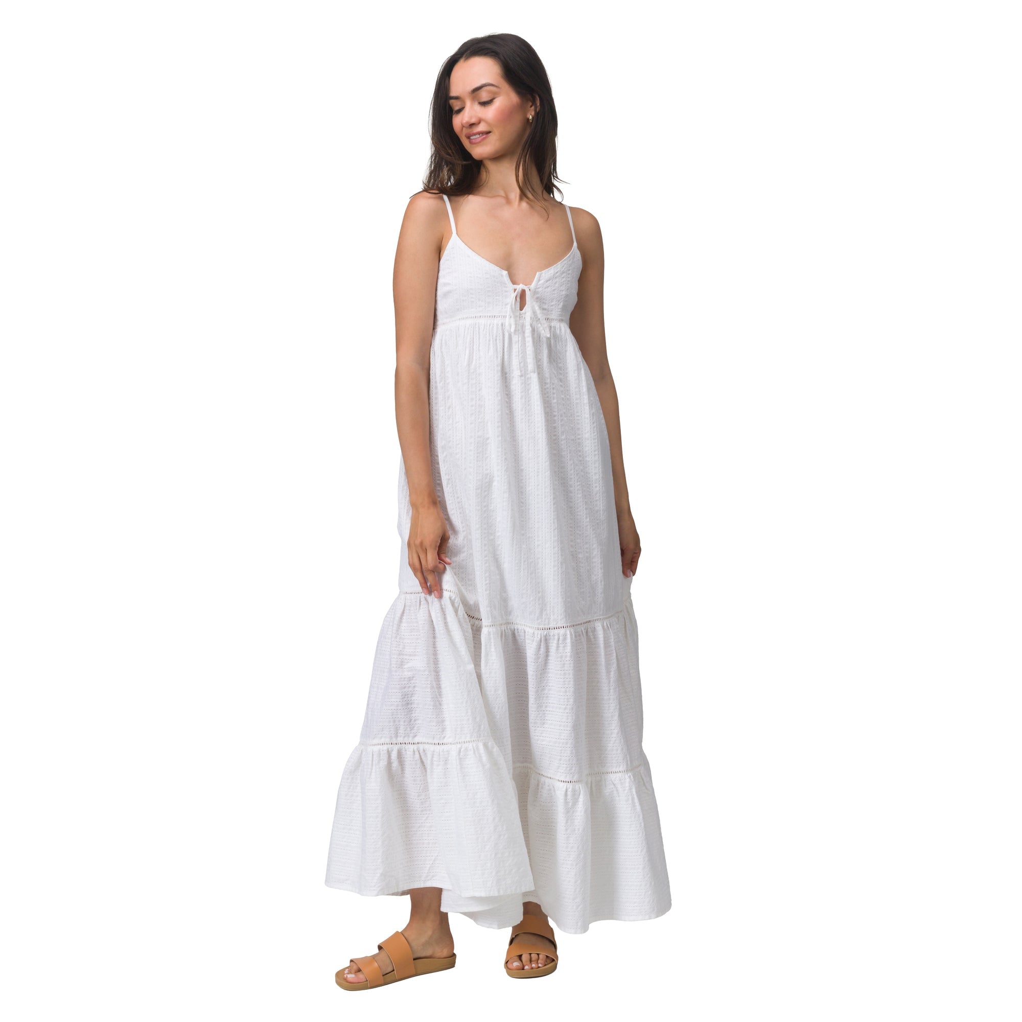 Woman wearing white Yuni Maxi Dress, standing and holding a dress hem, styled with tan sandals for beach comfort.