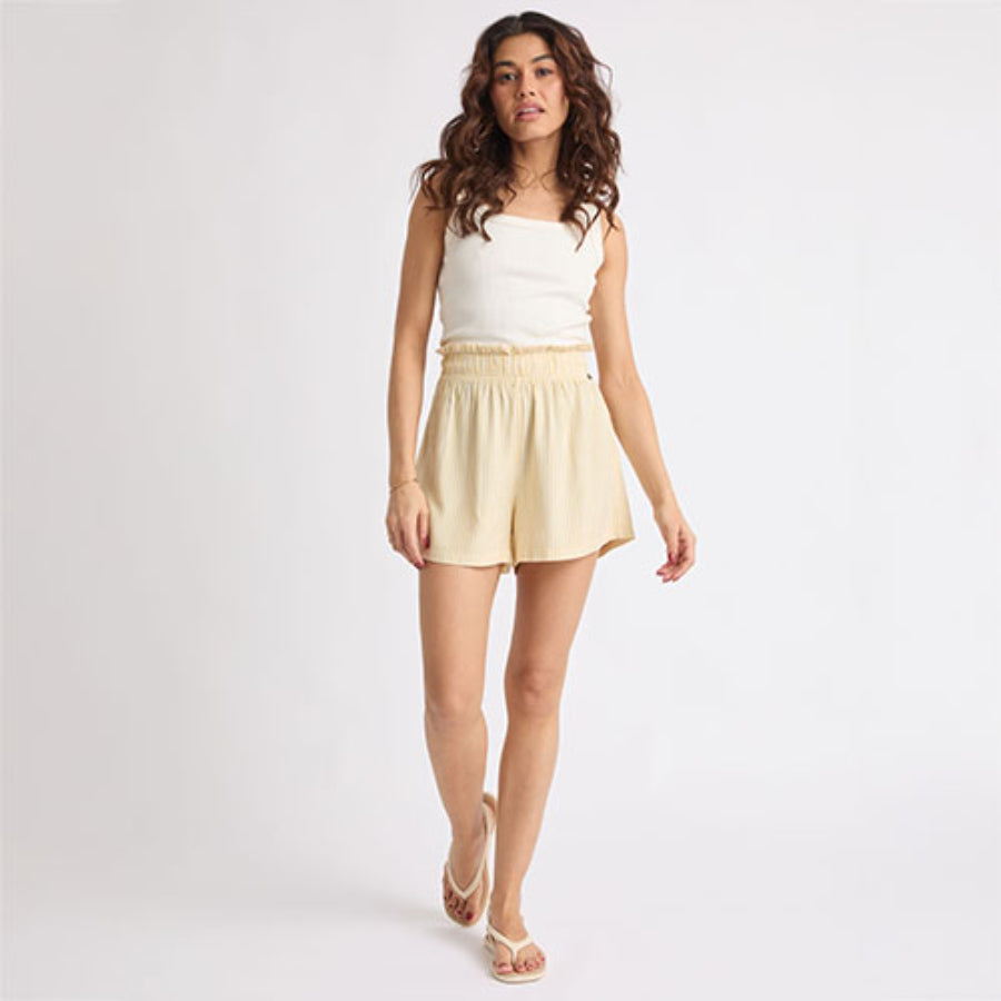 Woman wearing beige Ellie Short walking forward, paired with white sandals facing forward, showcasing beach-inspired comfort.
