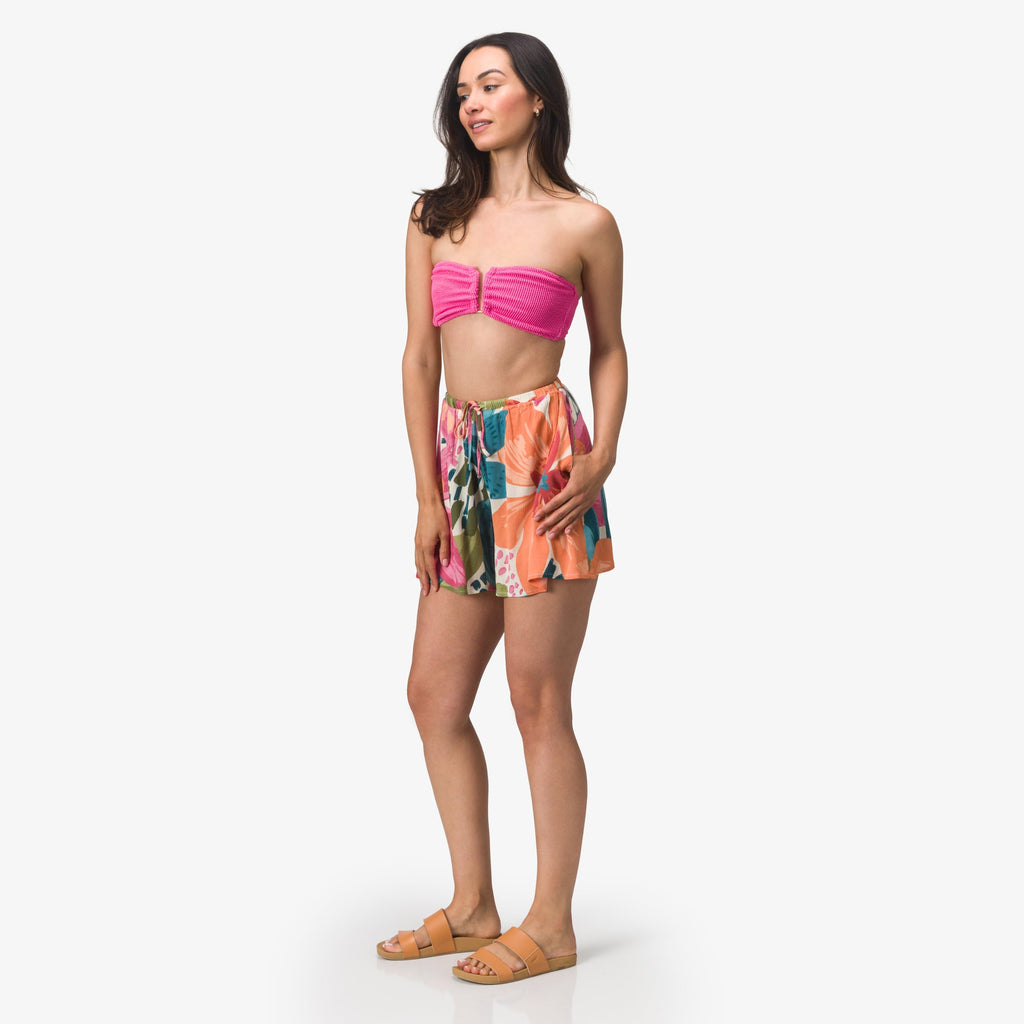 Woman wearing Eve Flutter Short with vibrant floral pattern standing facing left in casual beach apparel and sandals