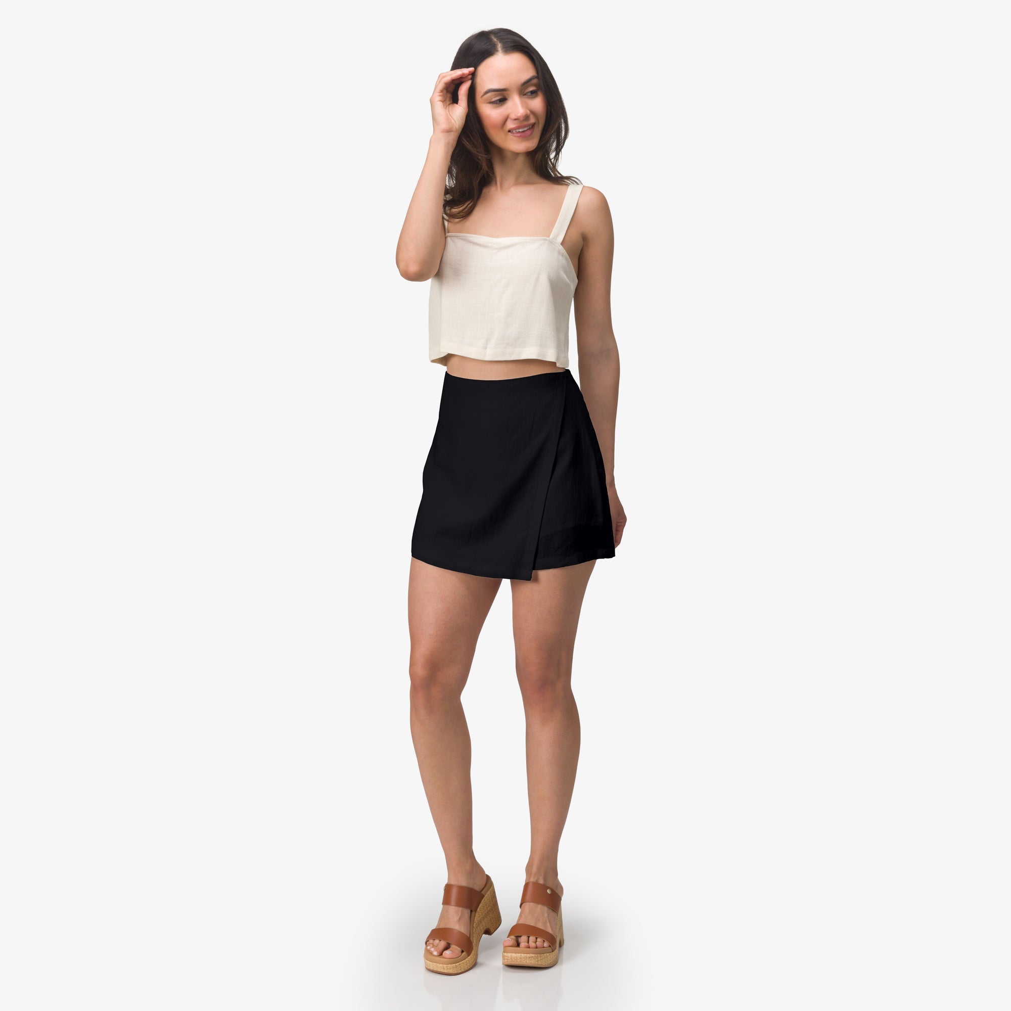 Woman wearing Tori Linen Wrap Skort in black, standing with brown platform sandals facing forward, beach-inspired comfort apparel
