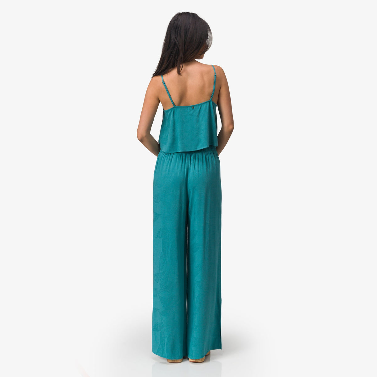 Woman facing away wearing teal Ollie Tank with loose, flowy beach-inspired pants and thin straps, comfortable casual apparel.