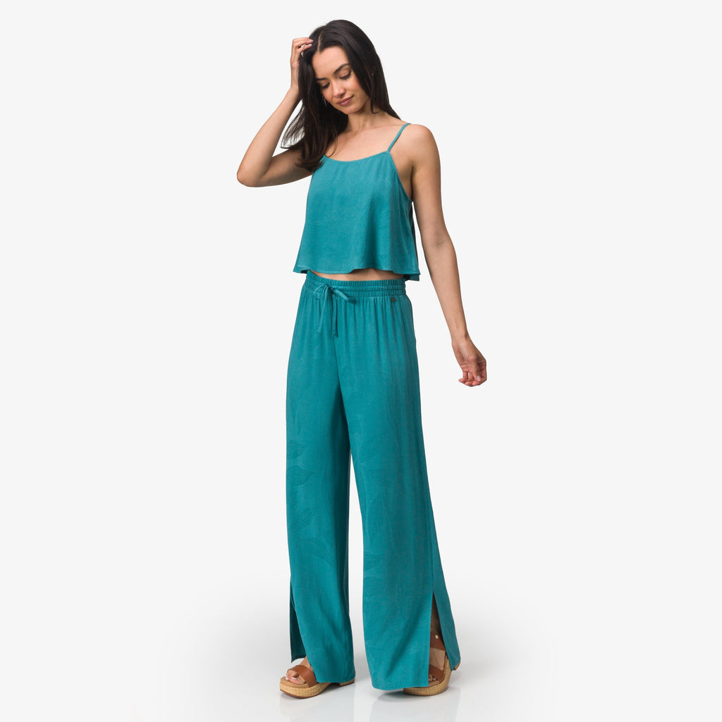 Woman wearing teal Ollie Tank and matching wide-leg pants, standing with hand on head, front view, beach-inspired comfort apparel