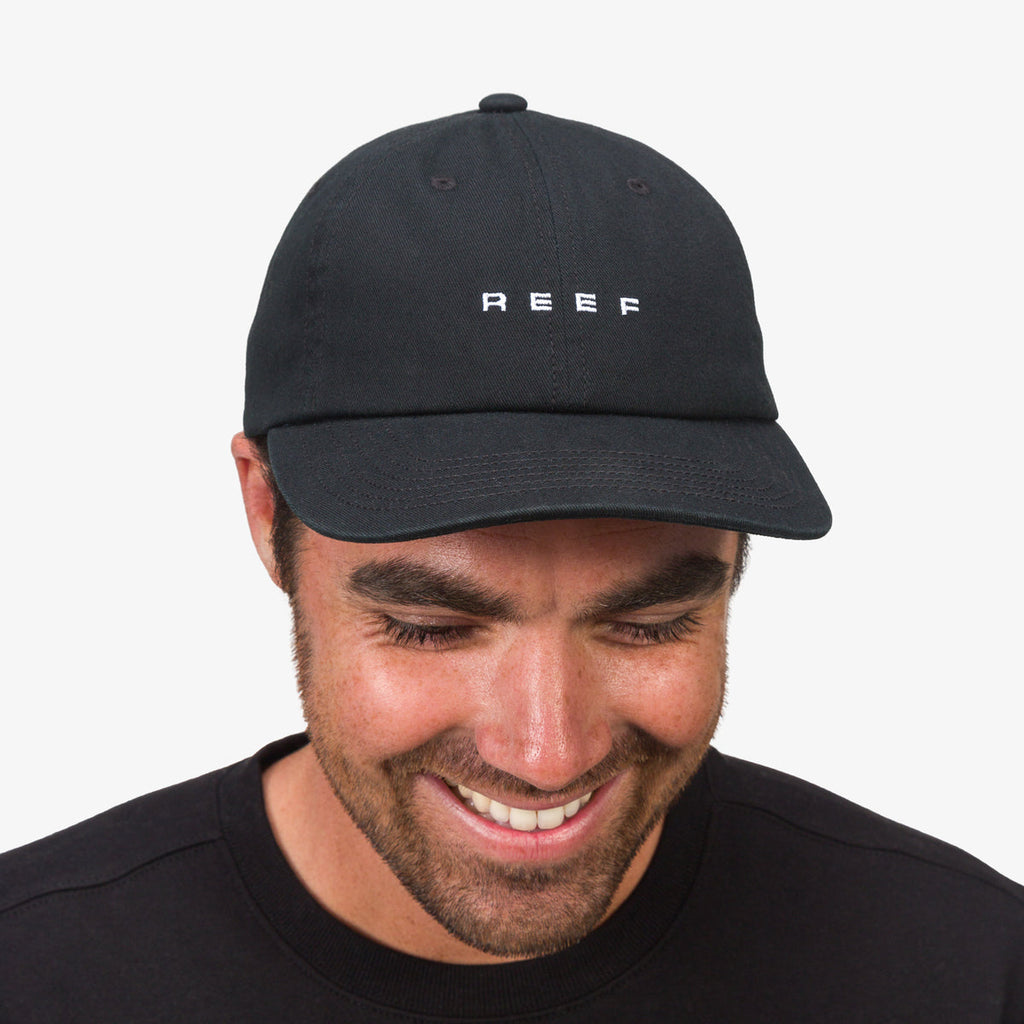 Front view of a man wearing a black Schotts Twill Hat with REEF logo, showcasing beach-inspired comfort and style.
