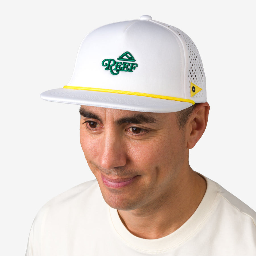 Man wearing a white Blackball Hat facing front with green REEF logo and yellow detailing, beach-inspired style.