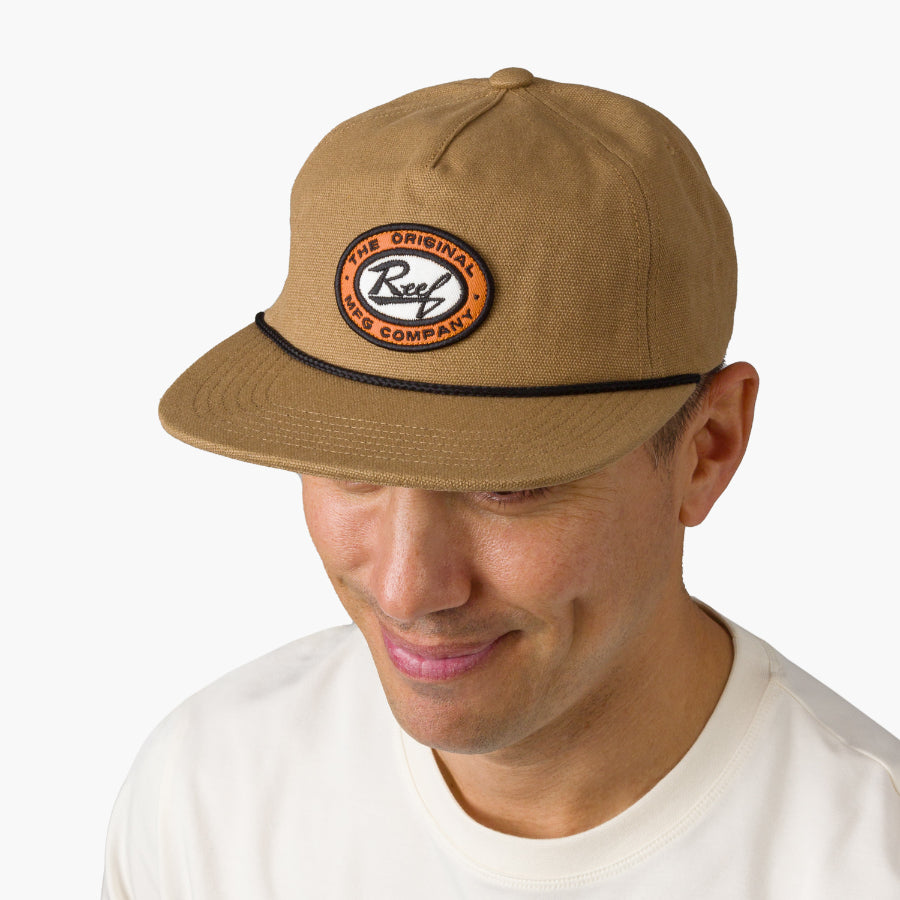 Man wearing a tan Trapper Hat facing forward, showcasing the front patch logo with comfort and beach-inspired style.