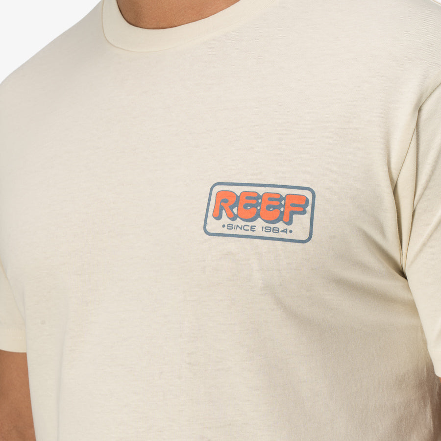 Close-up of the chest area of the Quinn Tee in cream featuring a REEF logo, surf-inspired and comfort-focused apparel.