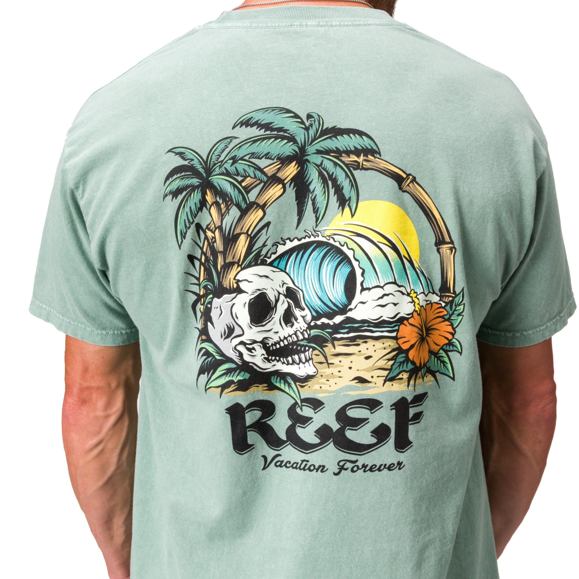 Akin Tee on a man, back view, featuring a beach graphic with palm trees, waves, a skull, and reef branding.