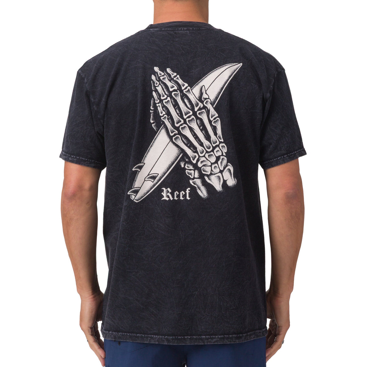 Rear view of men's Pray Tee in black featuring skeletal hands holding a surfboard, showcasing beach-inspired comfort apparel.